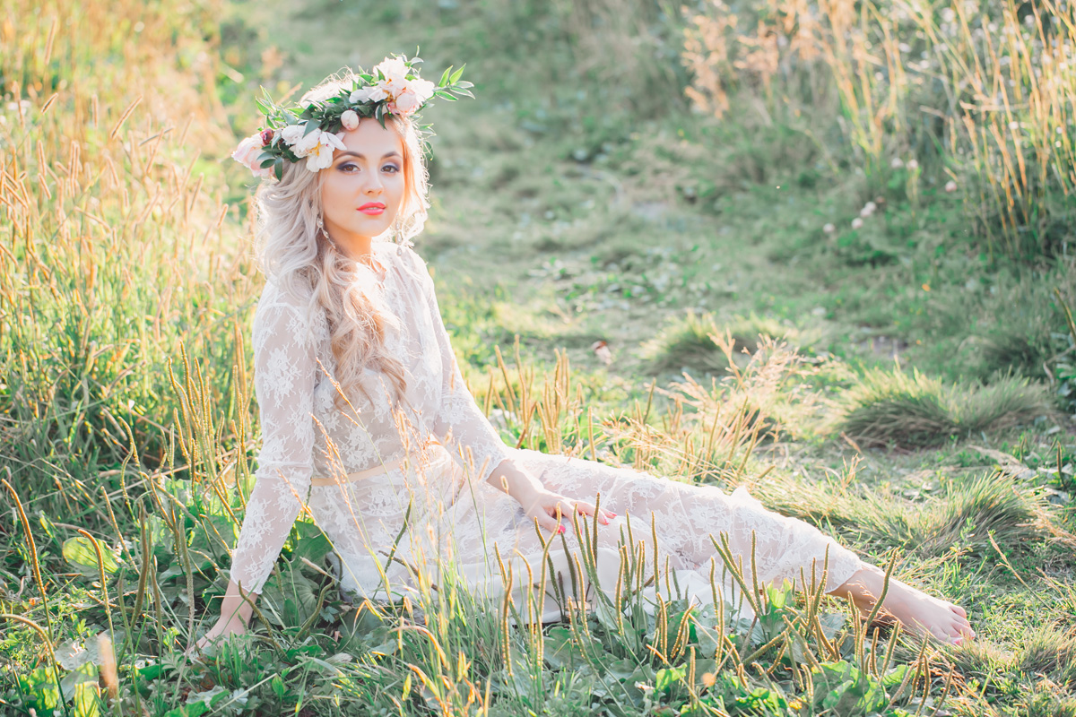 Bride with the flowers in her hair sits on the ground of the field